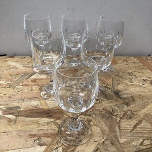 Peut inclure: Ensemble de six verres à vin en cristal transparent. Les verres ont un pied et un motif sur le bol. Les verres sont disposés sur une surface en bois.