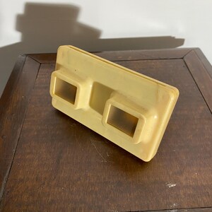 Peut inclure: Un vieux visionneur 3D en plastique blanc cassé avec deux fentes de visualisation rectangulaires. Le visionneur est conçu pour contenir des diapositives ou des cartes 3D.