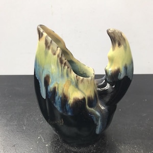 Könnte beinhalten: Eine keramische, krabbenförmige Vase mit glänzendem Finish. Die Vase hat einen schwarzen Sockel mit gelben, blauen und braunen Akzenten an der Klaue und der Oberseite. Das Wort "Finney" ist auf der Seite geschrieben.