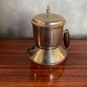 May include: A silver metal coffee pot with a wooden handle and a spout. The pot has a round body and a lid with a knob on top.