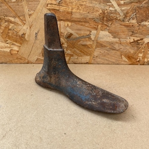 Puede incluir: Un antiguo molde de zapato de metal, utilizado por zapateros para dar forma a los zapatos. El molde está oxidado y tiene una pátina azul. Está hecho de hierro fundido y tiene una punta puntiaguda.