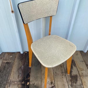 Peut inclure: Chaise vintage avec assise et dossier beige clair. La chaise a une structure en bois avec une finition naturelle et des pieds inclinés. Le dossier est rectangulaire avec une bordure noire. La chaise est sur une surface en bois.