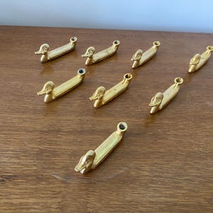 May include: Eight gold-toned duck-shaped drawer pulls. The pulls are all the same size and shape, and they have a simple, elegant design.