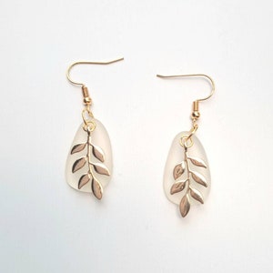 May include: A pair of gold-coloured leaf earrings. Each earring features a frosted teardrop-shaped pendant with a gold-coloured leaf design. The earrings have gold-coloured fish hook closures.