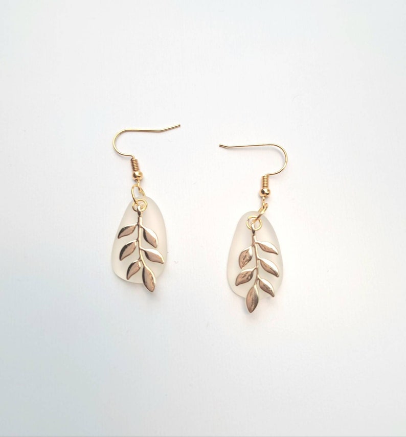 May include: A pair of gold-coloured leaf earrings. Each earring features a frosted teardrop-shaped pendant with a gold-coloured leaf design. The earrings have gold-coloured fish hook closures.