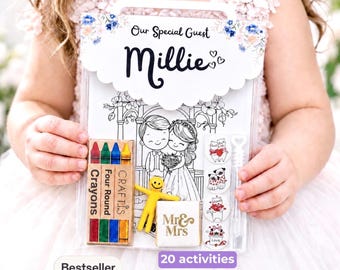 May include: A clear plastic activity pack labeled Our Special Guest Millie with a floral header. It contains a coloring book with a bride and groom illustration, a box of four round crayons, a yellow smiley figure, and four circular stickers.