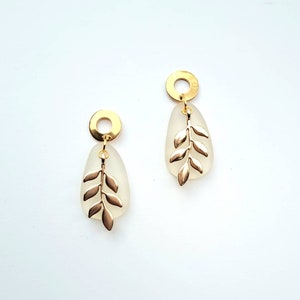 May include: A pair of gold-coloured earrings. Each earring has a gold-coloured circular top, a frosted teardrop-shaped pendant, and a gold-coloured leaf design. The earrings are displayed against a white background.