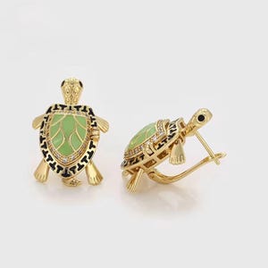 Puede incluir: Pendientes dorados con forma de tortuga, con caparazones de esmalte verde y detalles negros. Los pendientes presentan un diseño detallado con pequeños adornos brillantes. La cabeza y las patas de la tortuga también son doradas.