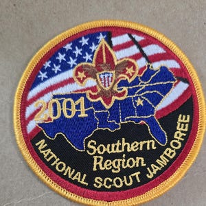 Op de afbeelding: Een ronde patch met een gouden rand. De patch heeft een rood, wit en blauw ontwerp met de tekst "2001 National Scout Jamboree Southern Region". Het ontwerp bevat een kaart van de zuidelijke Verenigde Staten en het logo van de Boy Scouts of America.