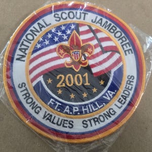 May include: Circular patch for the National Scout Jamboree 2001, featuring the American flag and a fleur-de-lis emblem. The patch includes text that reads "Strong Values Strong Leaders" and "Ft. A.P. Hill, VA."
