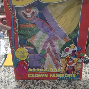 May include: A vintage clown costume set in a box. The box is red with yellow text that reads "CLOWN FASHIONS" and "16-18 INCH". The costume includes a hat, bib, pants, and shoes. The box also features a cartoon clown illustration.