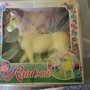 May include: A vintage Flower Princess Rainbow toy in its original packaging. The toy is a light yellow unicorn with a pink mane and a floral garland. The box features floral designs and the text "Fairytale Unicorn for 11" Fashion Dolls!"