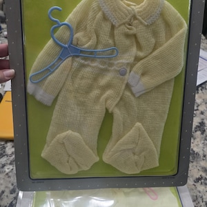 May include: A Dreamland Series baby doll outfit, designed for 16-18 inch dolls. The outfit includes a yellow romper with a white collar and cuffs, and a blue hanger. The packaging also shows a second outfit.