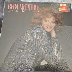 May include: A vinyl record album titled "Unlimited" by Reba McEntire. The album cover features a smiling woman with red hair wearing a sequined silver top. The album is sealed in plastic.