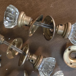 Op de afbeelding: Een verzameling vintage glazen deurknoppen met messing hardware. De knoppen zijn helder, facetgeslepen en hebben een klassieke, antieke uitstraling. De messing componenten vertonen tekenen van slijtage.