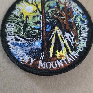 May include: Embroidered patch with a scenic mountain and camping design. The patch features a forest, waterfall, tent, and campfire, with text that reads "Smoky Mountain Fall Camporee Council". The patch is round with a black border.