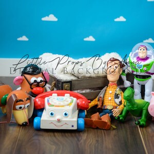 May include: A collection of toy characters from the Toy Story franchise, including Woody, Buzz Lightyear, Slinky Dog, Mr. Potato Head, Rex, and a piggy bank. The toys are arranged on a wooden floor in front of a blue wall with white clouds.