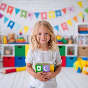 Może przedstawiać: Małe dziecko trzymające książki z kolorowymi klockami ABC w klasie. Pokój posiada baner z literami, globus i różne zabawki, tworząc zabawne środowisko uczenia się. Tło obejmuje białe półki i kolorowe pojemniki do przechowywania.