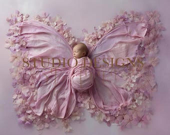 May include: A newborn baby swaddled in pink fabric, posed as a butterfly, surrounded by pink flowers. The baby is nestled in the center of the butterfly wings, with the text "STUDIO DESIGNS" in gold lettering.