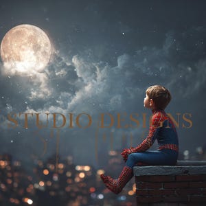 May include: A child in a Spider-Man costume sits on a brick ledge, gazing at a full moon in a night sky filled with stars. The city lights glow in the background, with the words "STUDIO DESIGNS" in the image.