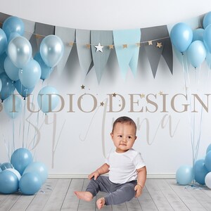 May include: A baby boy wearing a grey outfit sits in front of a blue and grey balloon arch with the text "Studio Designs by Tina".