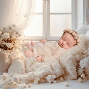 May include: A newborn baby wearing a white dress and a flower crown sleeps on a white bed with a white blanket. The baby is surrounded by white flowers and a white stuffed animal.