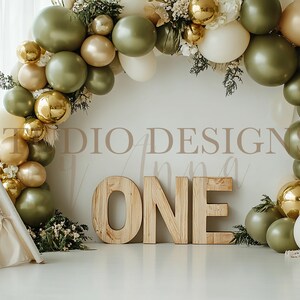 May include: A white teepee tent with a green and gold balloon arch behind it. The balloons are in shades of green, gold, and white. The arch is decorated with greenery and the word "ONE" is displayed in front of the arch.