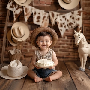 Può includere: Un bambino sorridente con cappello da cowboy e pantaloncini di jeans, che tiene in mano una piccola torta su un piatto. Lo sfondo presenta un pavimento in legno rustico, un muro di mattoni e cappelli da cowboy. Una statua di cavallo bianco è sulla destra.