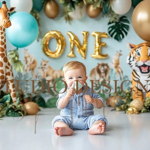 Puede incluir: Un bebé con un atuendo azul se sienta frente a un telón de fondo con temática de jungla con juguetes de peluche de jirafa y tigre. Globos dorados deletrean "ONE". También hay globos dorados, blancos y turquesas. El bebé sostiene un dulce.