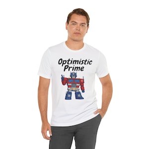 May include: White t-shirt with the text "Optimistic Prime" above a cartoon image of a red, blue, and silver robot giving a peace sign. The robot is a stylized version of Optimus Prime.