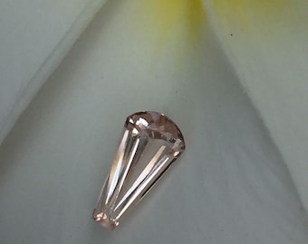 Puede incluir: Una piedra preciosa facetada de color rosa pálido con una punta puntiaguda, que se asemeja a una lágrima.