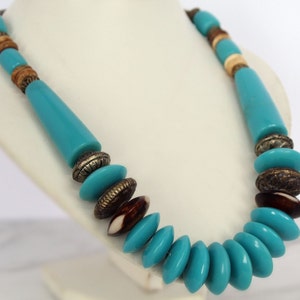 Può includere: Una collana di perline turchesi e marroni con accenti argentati. La collana presenta una varietà di forme e dimensioni di perline, tra cui perline rotonde, ovali e cilindriche.