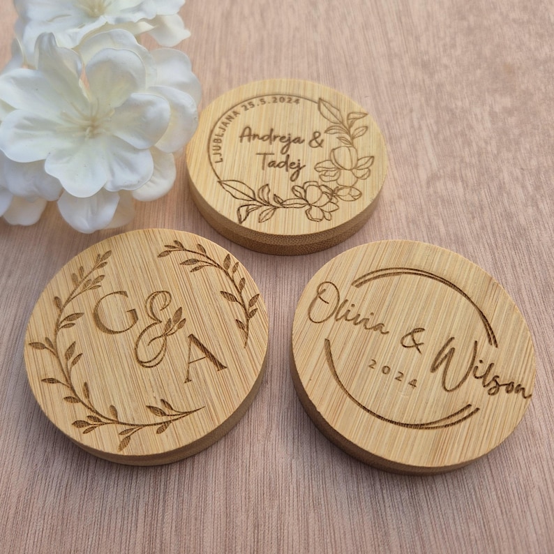 May include: Three circular wooden coasters with engraved details. One coaster displays the names "Andreja & Tadej" and the date "25.5.2024". Another has the initials "G & A", and the third says "Olivia & Wilson 2024".