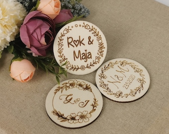May include: Three round wooden signs with floral designs and engraved text. The first sign says "Rok & Maja" with a heart symbol. The second sign says "N & M 23.02.2020". The third sign says "Y & J".
