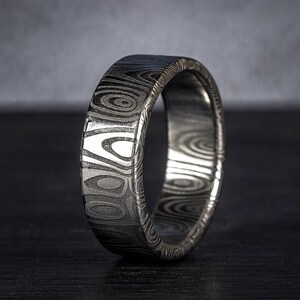 Puede incluir: Primer plano de un anillo plateado con un patr&oacute;n &uacute;nico. El anillo tiene una superficie texturizada con dise&ntilde;os org&aacute;nicos y arremolinados. El anillo es de metal y tiene un acabado pulido. Es una joya.