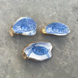 May include: Three oyster shells painted with gold trim and a blue and white sea turtle design.