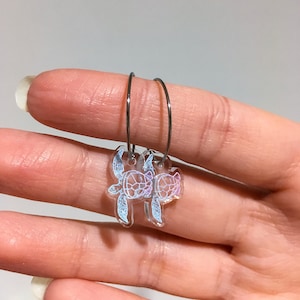 May include: A pair of silver hoop earrings with a clear iridescent turtle charm hanging from each hoop.
