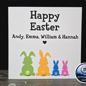 May include: A white card with the text "Happy Easter" and the names "Andy, Emma, William & Hannah". Four colourful paper bunny silhouettes with buttons are at the bottom of the card. The card is from Button Loon Cards.