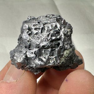 以下が含まれることがあります： 表面がざらざらした、灰色で金属製の隕石のクローズアップ。