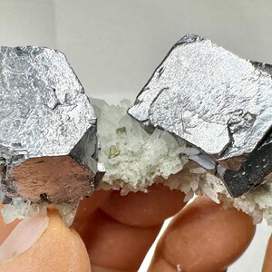 May include: A mineral specimen featuring two large, metallic, silver-gray cubic galena crystals attached to a cluster of smaller, white, translucent quartz crystals. The galena crystals exhibit a distinct, reflective, blocky structure.