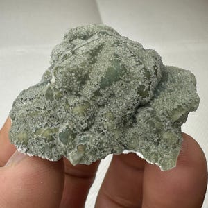 Op de afbeelding: Een groene en witte kristalkluster met een ruw, getextureerd oppervlak. De kristal heeft een natuurlijke, organische vorm en is een prachtig voorbeeld van een mineraal specimen.