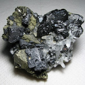 May include: A cluster of black and gray galena crystals with a silvery sheen, surrounded by clear quartz crystals and a matrix of brassy pyrite.