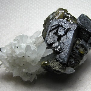 May include: A cluster of gray and black galena crystals with a few green and brown pyrite crystals. The galena crystals are clustered around a group of clear quartz crystals.