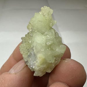 Puede incluir: Un cúmulo de cristales de color verde pálido y blanco, que se asemeja a una pequeña flor delicada.