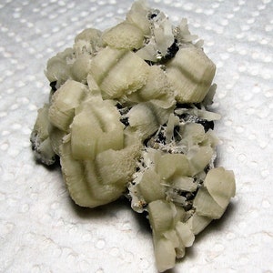 May include: A cluster of white and green mineral crystals with a striated pattern. The crystals are arranged in a random, organic shape.