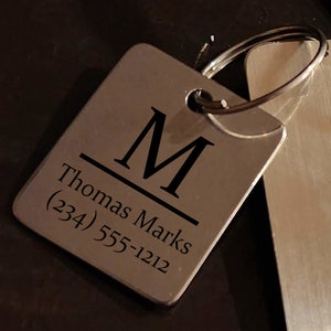 May include: Silver keychain with a square tag engraved with the letter "M", the name "Thomas Marks", and the phone number (234) 555-1212.