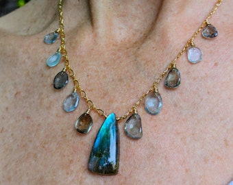 May include: A gold chain necklace with a large blue teardrop-shaped pendant and smaller teardrop-shaped stones in shades of blue and brown.