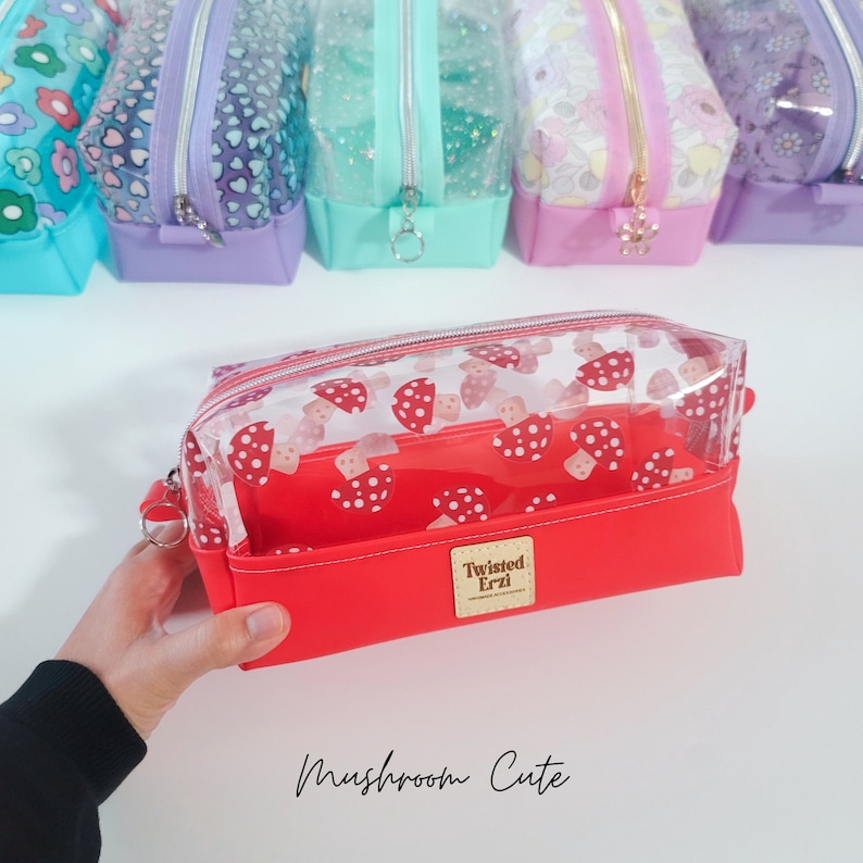 May include: A clear red makeup bag with a white mushroom print. The bag has a zipper closure and a small label that says "Twisted Erzi" on the front. The bag is labelled "Mushroom Cute".