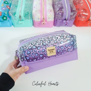May include: A clear purple pencil case with a zipper closure and a colourful heart pattern. The case has a clear plastic window and a label that says "Twisted Erzi". The text "Colorful Hearts" is printed below the case.