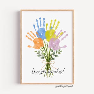 Peut inclure: Une impression encadrée représentant un bouquet de mains peintes à l'aquarelle en bleu, orange, jaune et violet. Des feuilles vertes et un nœud en ficelle ornent les fleurs d'empreintes de mains. Le texte "Love you bunches!" est écrit en dessous.